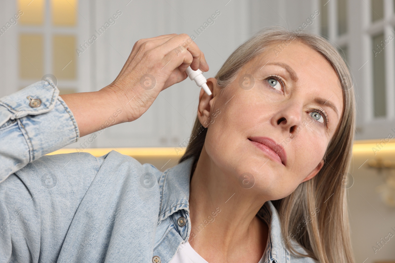 Photo of Woman applying medical ear drops at home