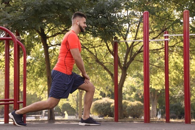 Young man with wireless headphones listening to music while exercising on sports ground. Space for text