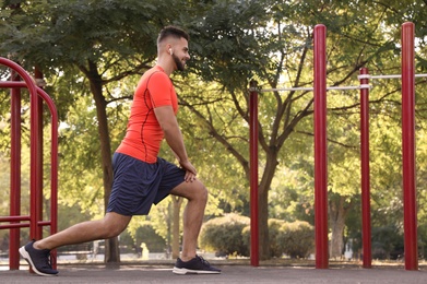 Photo of Young man with wireless headphones listening to music while exercising on sports ground. Space for text