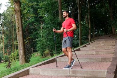 Photo of Man practicing Nordic walking with poles on steps outdoors, low angle view. Space for text