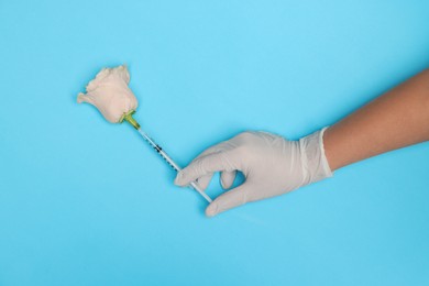 Photo of Doctor making injection to rose on light blue background, top view