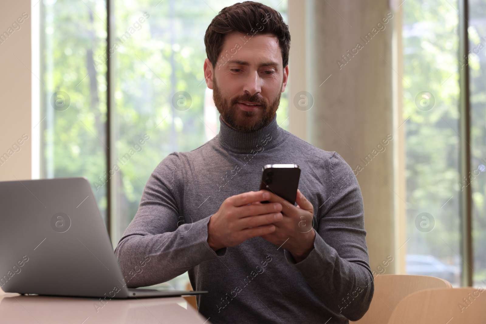 Photo of Handsome man using smartphone at table in cafe