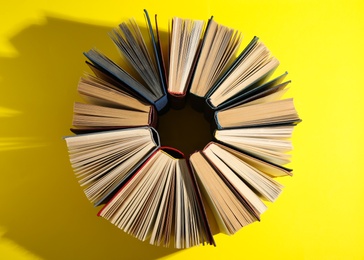 Circle made of hardcover books on yellow background, flat lay