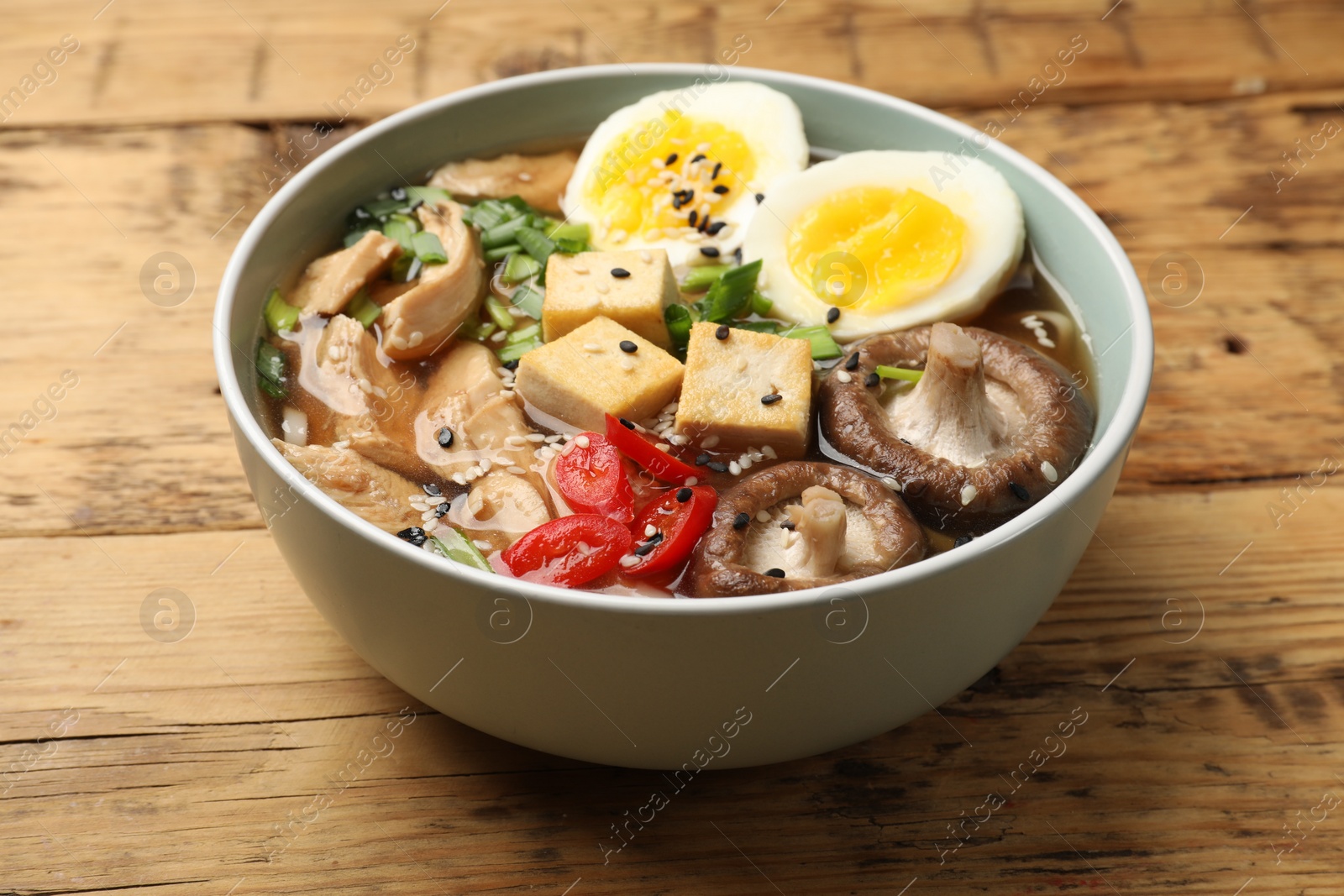 Photo of Bowl of delicious ramen on wooden table, closeup. Noodle soup