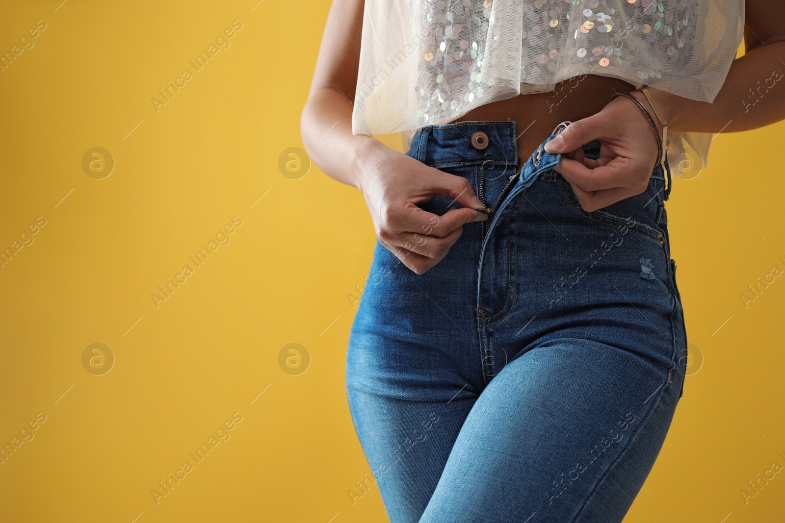 Photo of Woman unzipping jeans on yellow background, closeup. Space for text