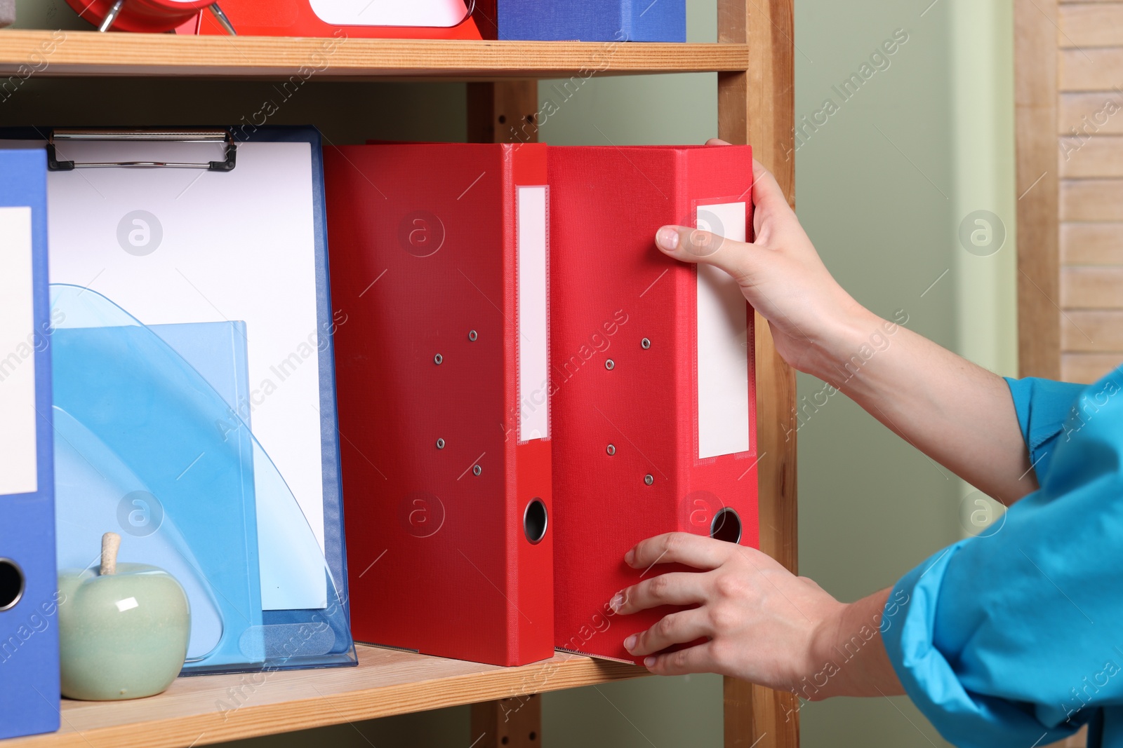 Photo of Woman taking binder office folder from shelving unit indoors, closeup