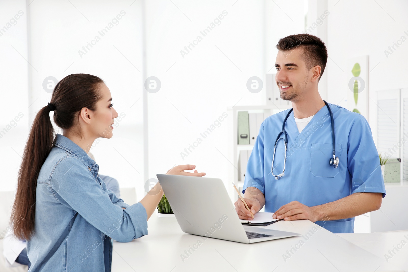 Photo of Young male doctor working with client at reception desk in hospital