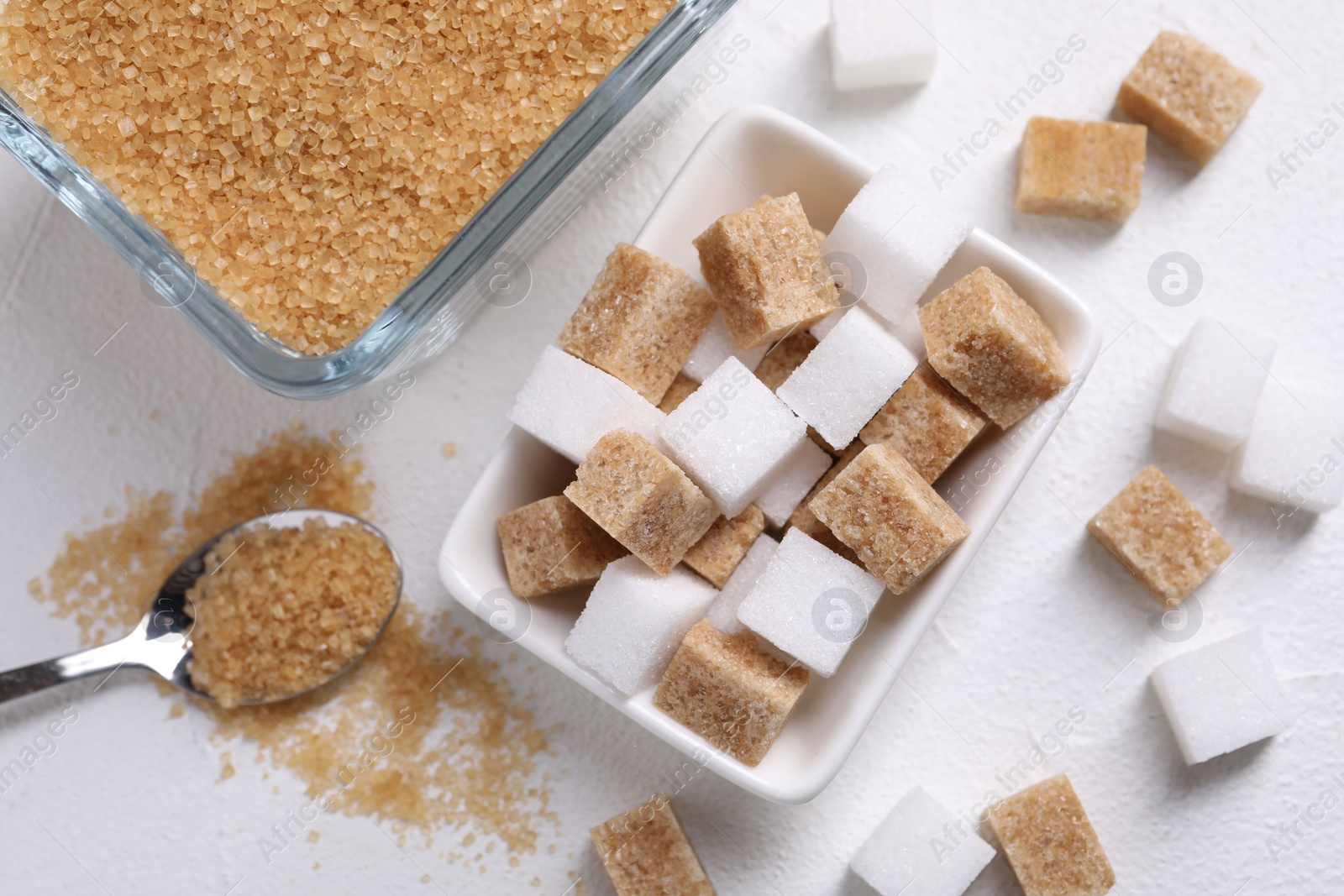 Photo of Bowls and spoon with different types of sugar on white table, flat lay