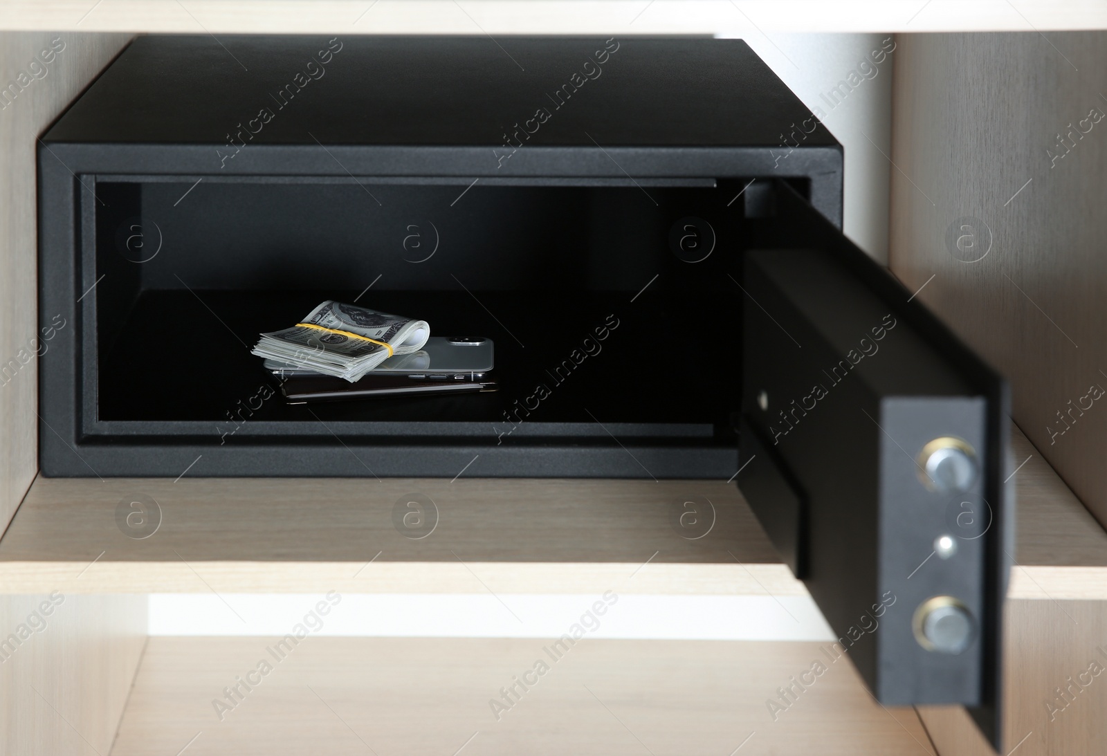 Photo of Open steel safe with money and smartphone in wooden closet