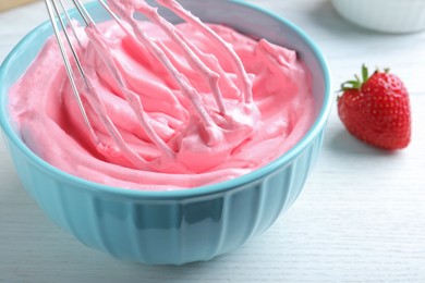 Photo of Whipping strawberry cream with balloon whisk on white wooden table, closeup