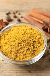 Photo of Curry powder in bowl and other spices on wooden table, closeup
