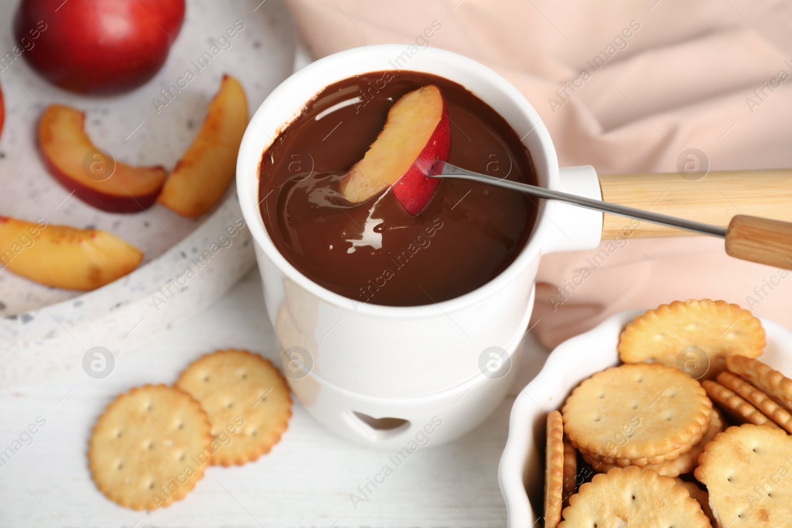 Photo of Fondue pot with chocolate and peach on white wooden table