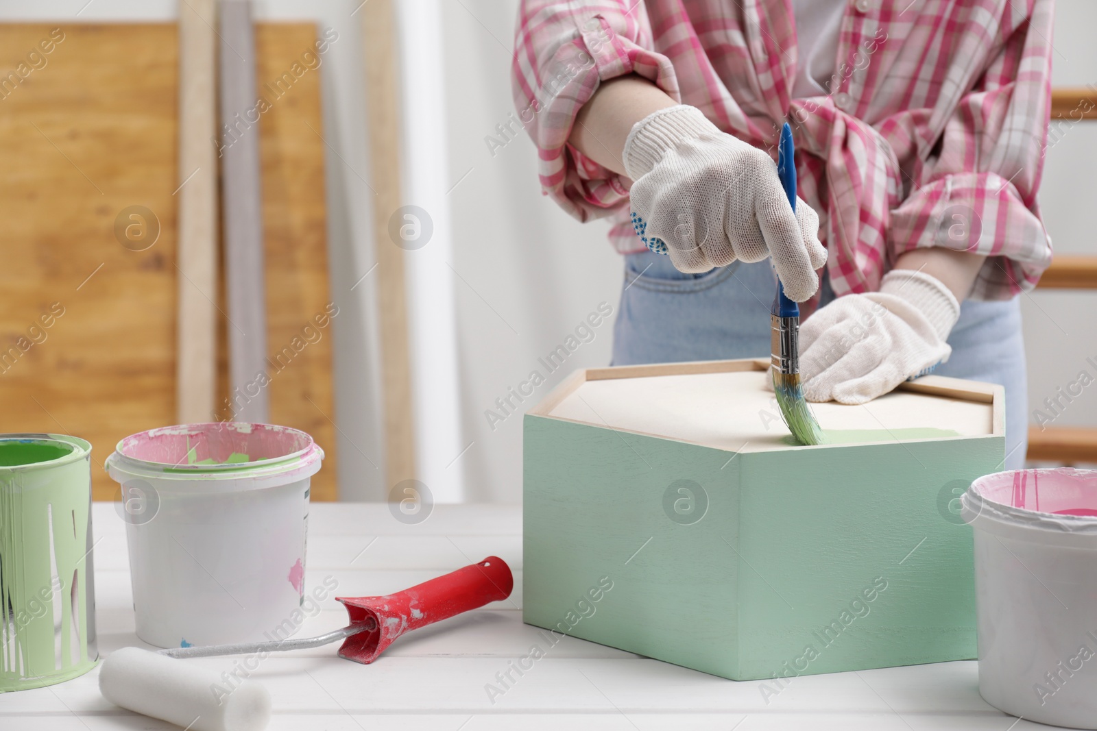 Photo of Woman painting honeycomb shaped shelf with brush at white table indoors, closeup