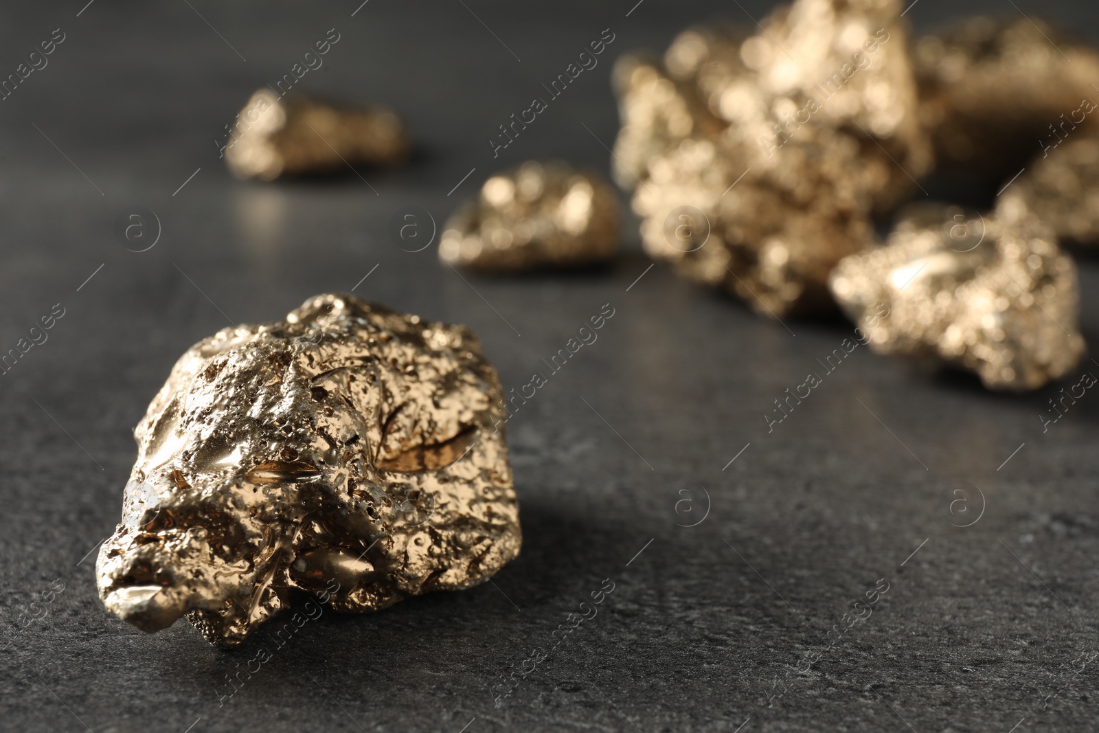 Photo of Shiny gold nugget on grey surface, closeup. Space for text