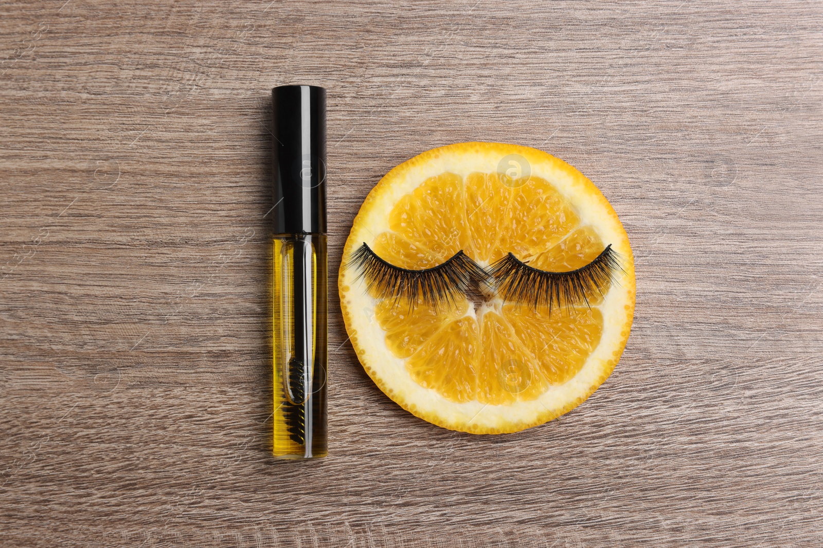 Photo of False eyelashes, orange slice and tube of oil on wooden table, flat lay