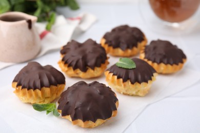 Delicious profiteroles with chocolate spread and mint on white table, closeup