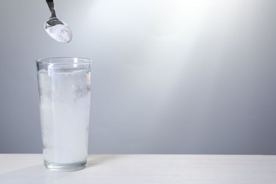 Photo of Adding baking soda into glass of water at white table against light grey background. Space for text