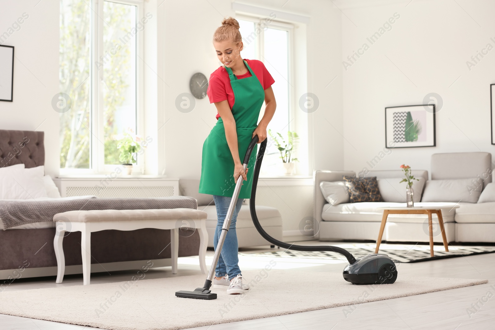 Photo of Woman removing dirt from carpet with vacuum cleaner indoors