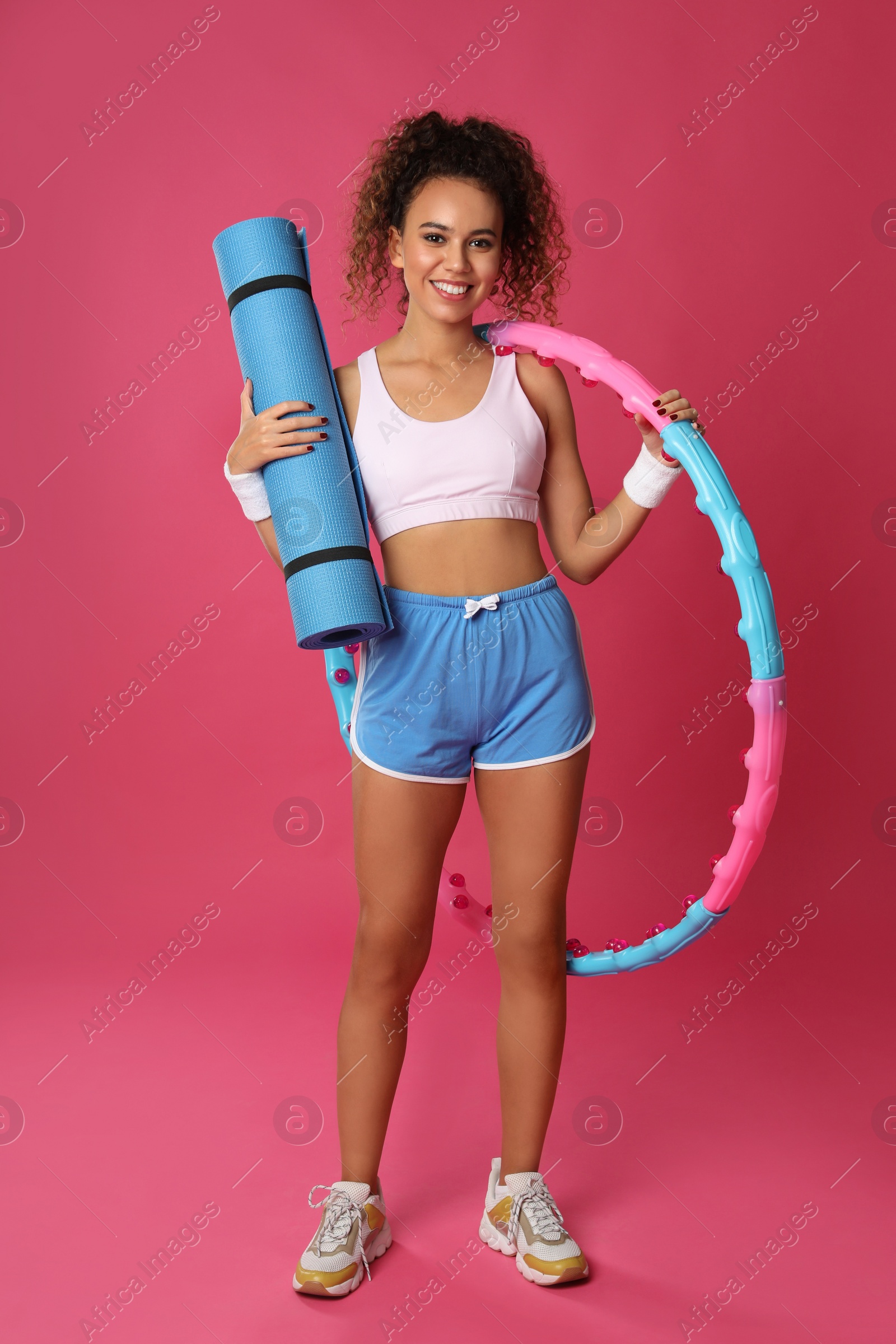 Photo of Beautiful African American woman with yoga mat and hula hoop on pink background