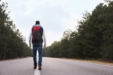 Man with backpack going along road near forest, back view