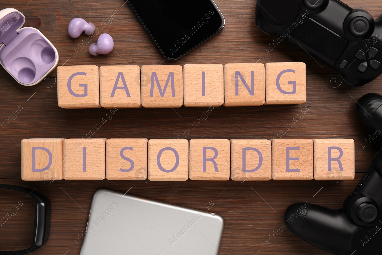 Photo of Phrase Gaming Disorder made of cubes and different devices on wooden table, flat lay. Addictive behavior