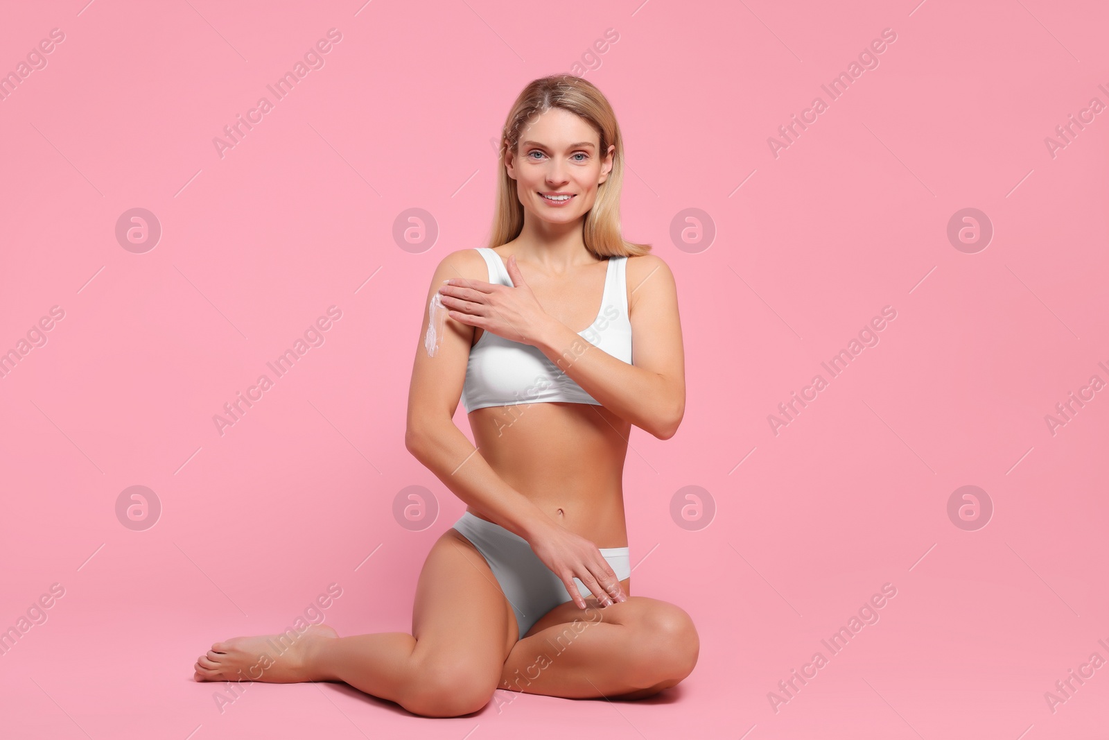 Photo of Woman applying body cream onto her arm against pink background