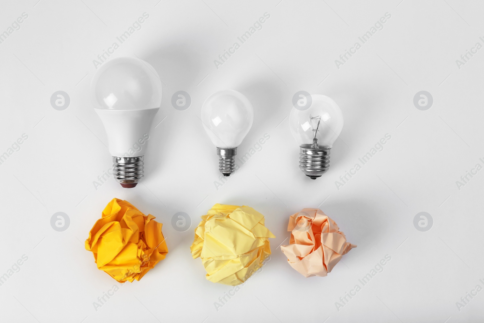 Photo of Composition with lamp bulbs and crumpled paper balls on white background, top view. Creative concept