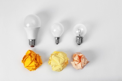 Photo of Composition with lamp bulbs and crumpled paper balls on white background, top view. Creative concept