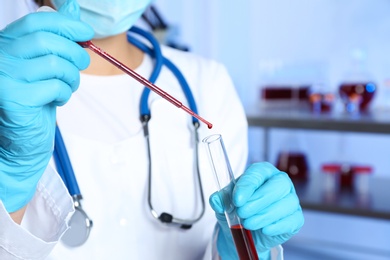 Laboratory worker pipetting blood sample into test tube for analysis, closeup