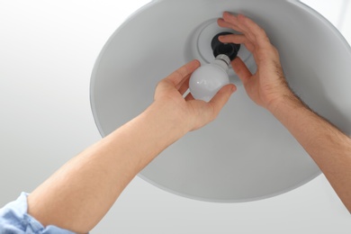 Photo of Man changing light bulb in lamp indoors, closeup