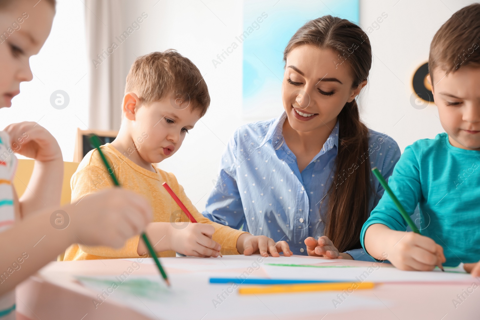 Photo of Little children with kindergarten teacher drawing at table indoors. Learning and playing