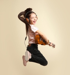 Emotional little girl with headphones playing guitar on color background