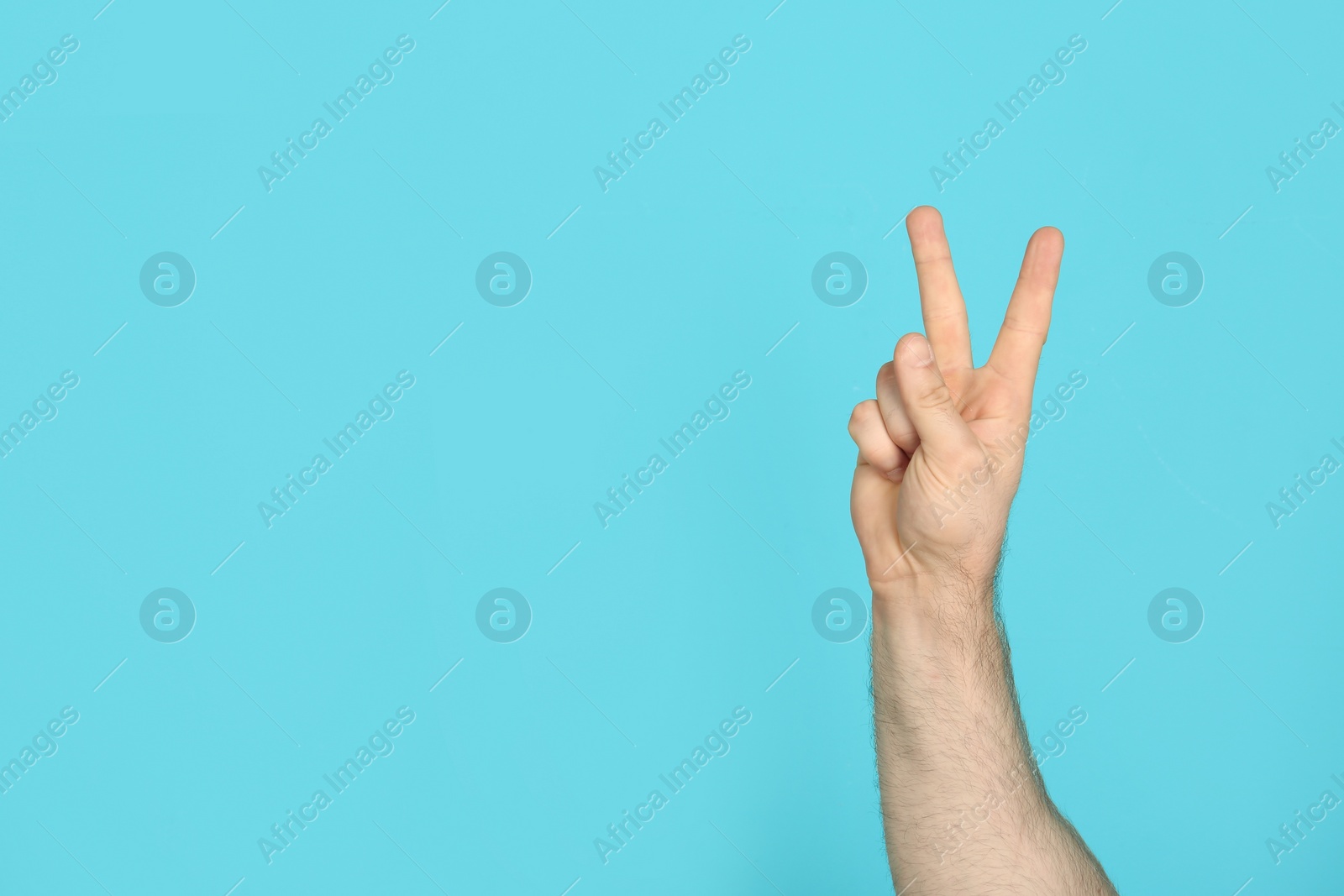 Photo of Young man showing victory gesture on color background. Space for text