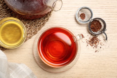 Photo of Freshly brewed rooibos tea, dry leaves and honey on wooden table, flat lay