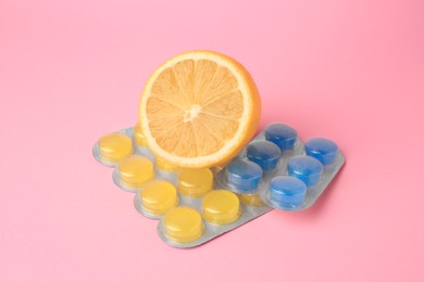 Photo of Blisters with cough drops and fresh lemon on pink background