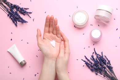 Photo of Woman applying hand cream and lavender flowers on pink background, top view