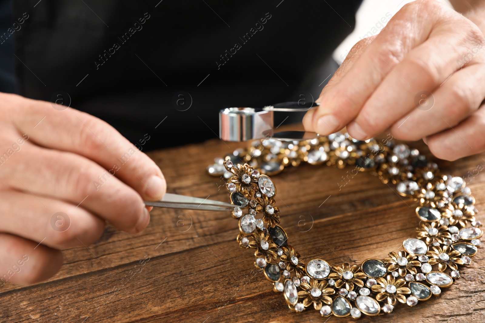 Photo of Male jeweler evaluating necklace at table in workshop, closeup