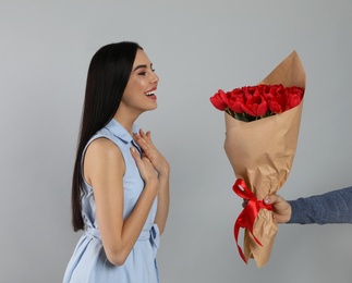 Photo of Happy woman receiving red tulip bouquet from man on light grey background. 8th of March celebration