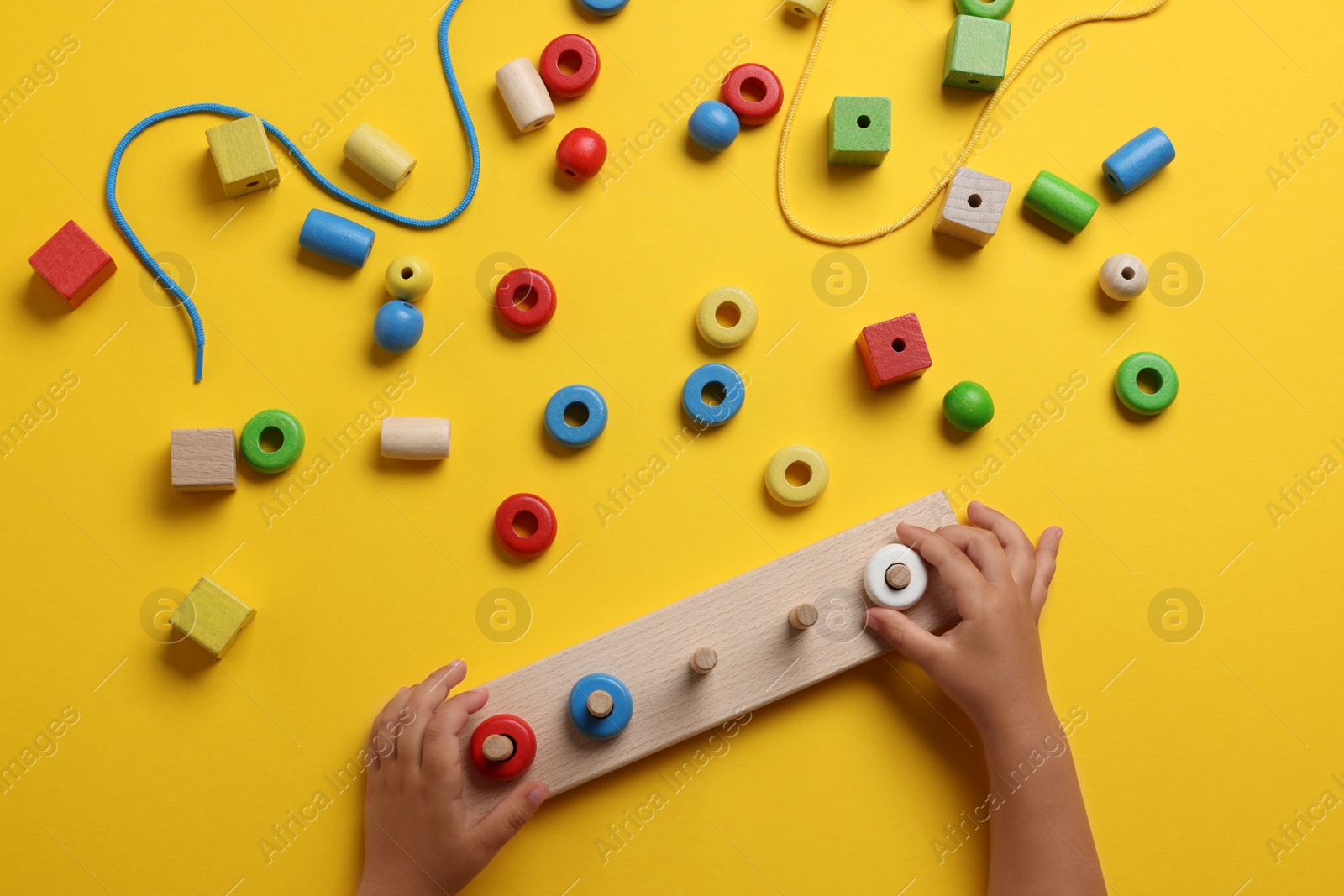 Photo of Motor skills development. Little child playing with stacking and counting game at yellow table, top view