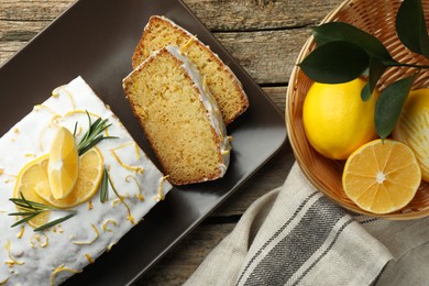 Tasty lemon cake with glaze and citrus fruits on wooden table, flat lay