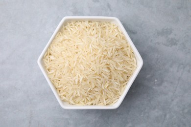 Raw rice in bowl on light grey table, top view