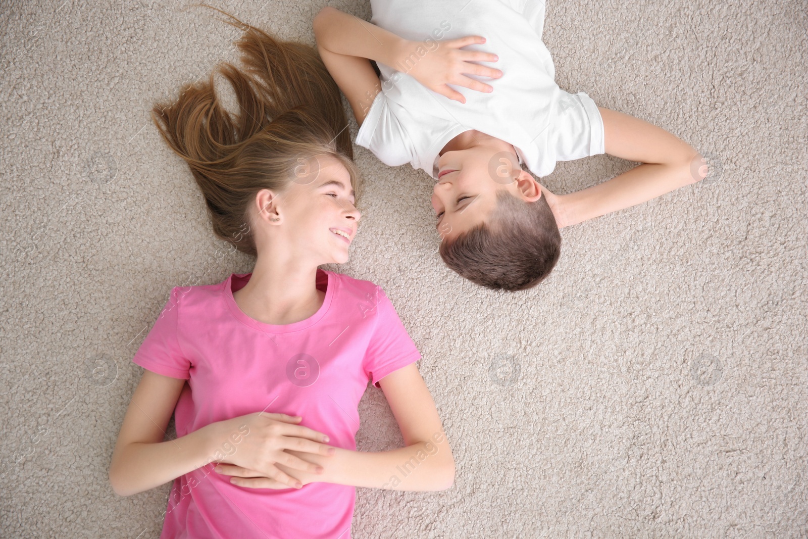 Photo of Teenage girl and her brother lying on cozy carpet at home, top view