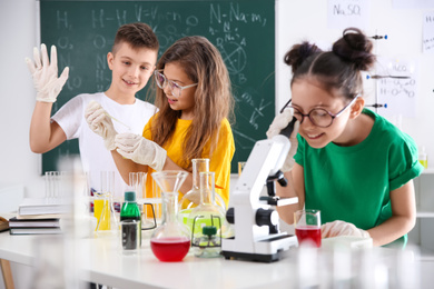 Photo of Schoolgirl looking through microscope and her classmates at chemistry class