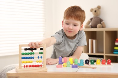 Photo of Happy little boy playing with abacus at desk in room. Learning mathematics with fun