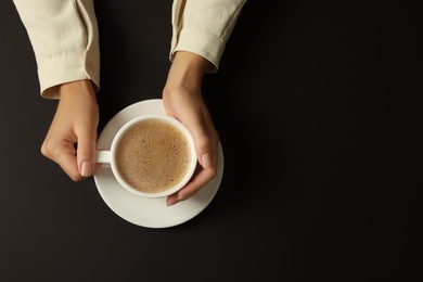 Woman with cup of coffee on black background, top view. Space for text