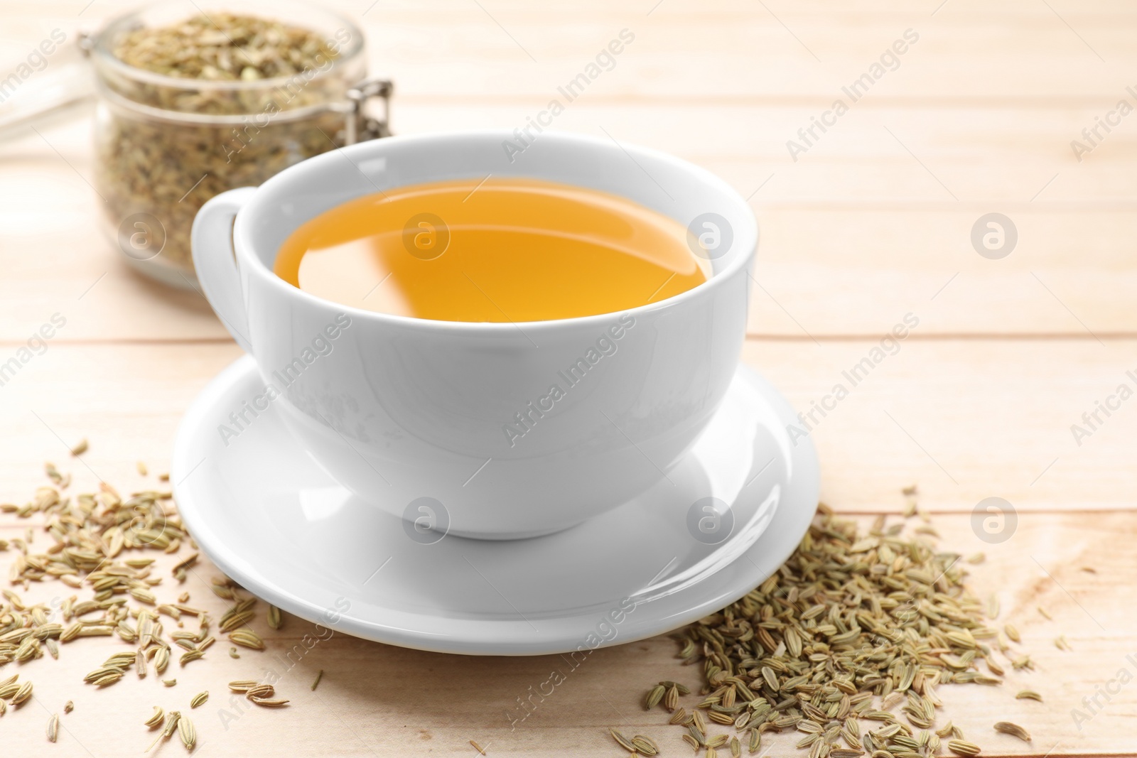 Photo of Fennel tea in cup and seeds on light wooden table, closeup