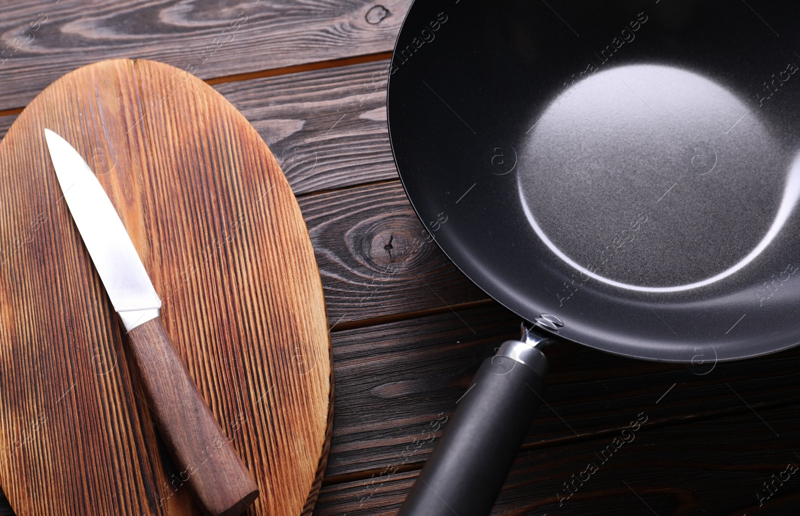 Photo of Empty iron wok, knife and cutting board on wooden table