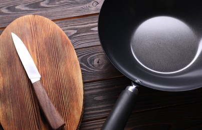 Empty iron wok, knife and cutting board on wooden table