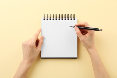 Photo of Woman writing in notebook on beige background, top view