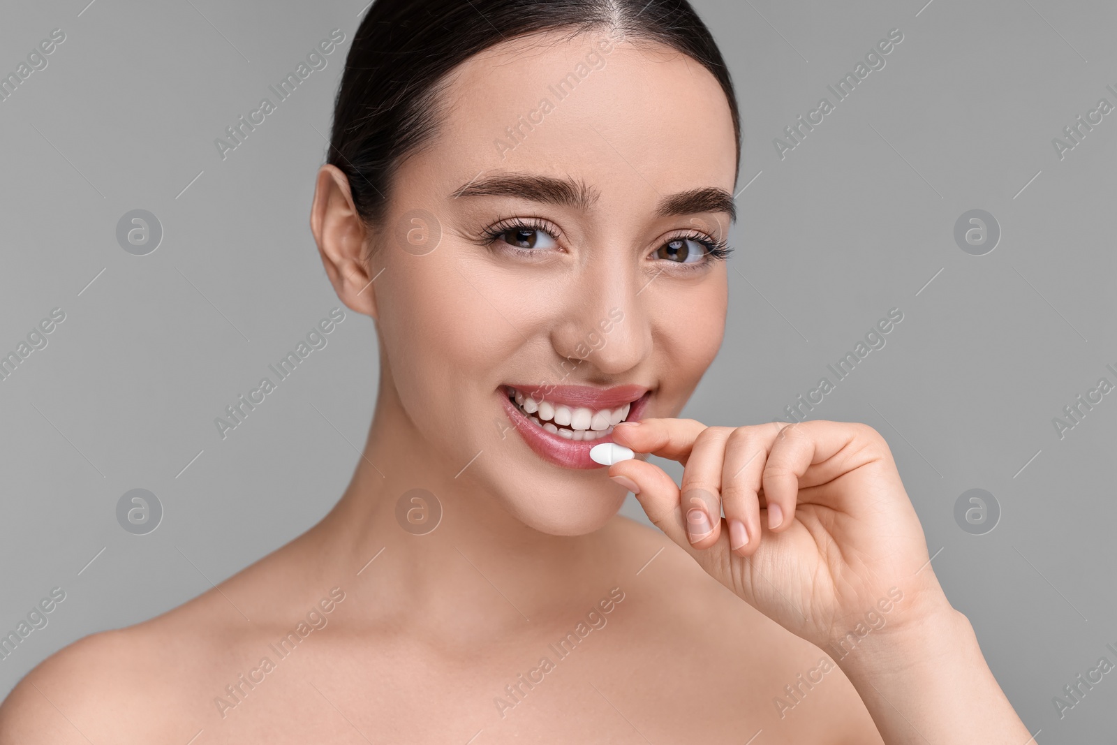 Photo of Beautiful young woman with vitamin pill on grey background